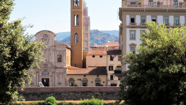 A historic building with a prominent tower, a river in the foreground, and a mountainous backdrop. - Hotel Relais Il Cestello (Florence)