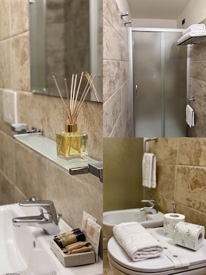 A bathroom with a marble wall, a glass shower enclosure, a sink with a mirror, and a toilet with a towel and toilet paper. - Hotel Relais Il Cestello (Florence)