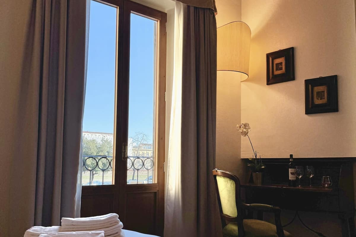 A hotel room with a bed, a desk, a chair, a lamp, and a window with curtains.