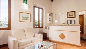A living room with a white sofa, a glass coffee table, and a white reception desk. - Hotel Relais Il Cestello (Florence)