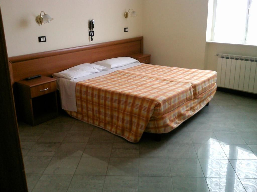 Un dormitorio con cama, mesita de noche, lámpara y ventana.