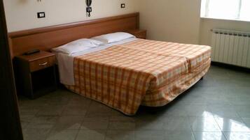 Un dormitorio con cama, mesita de noche, lámpara y ventana.