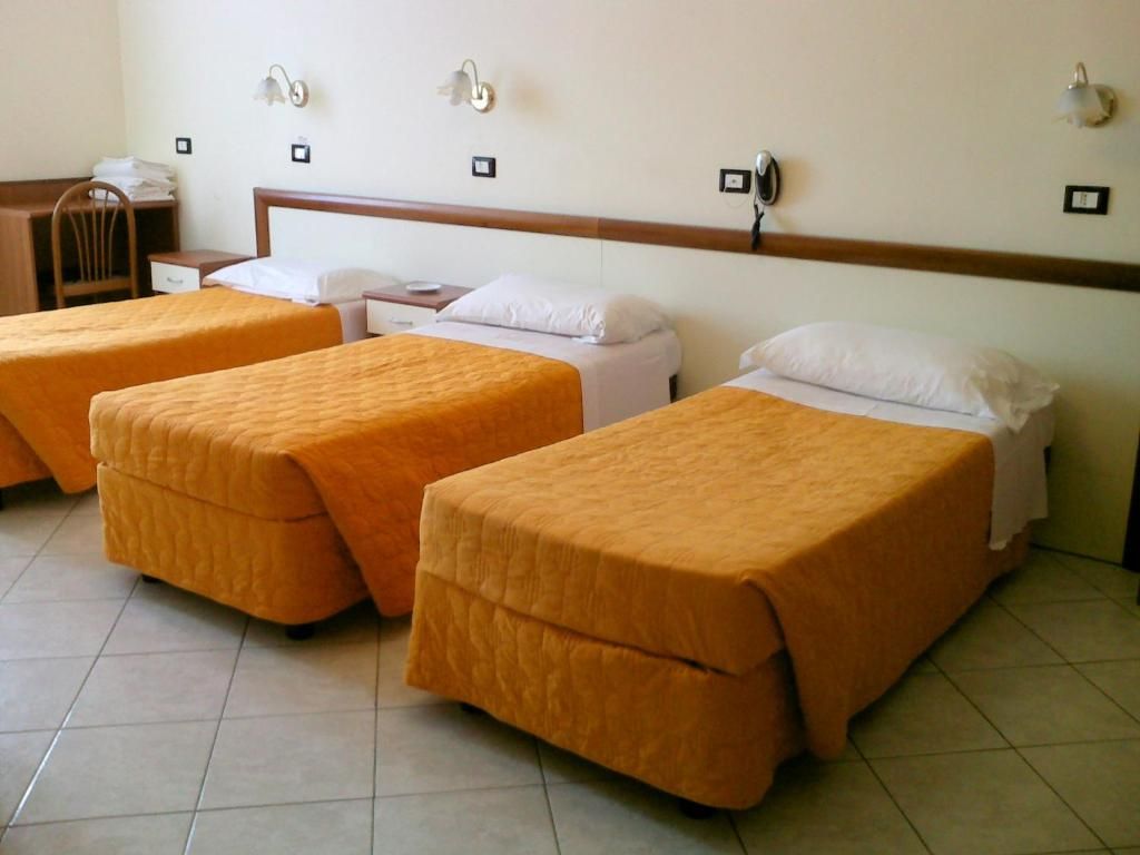 A hotel room with three single beds, a desk, and a chair.