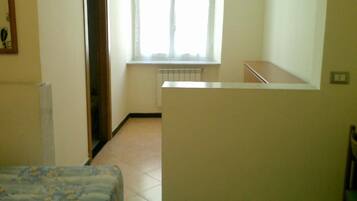 Una habitación con cama, un radiador, una ventana con cortinas y una escalera.