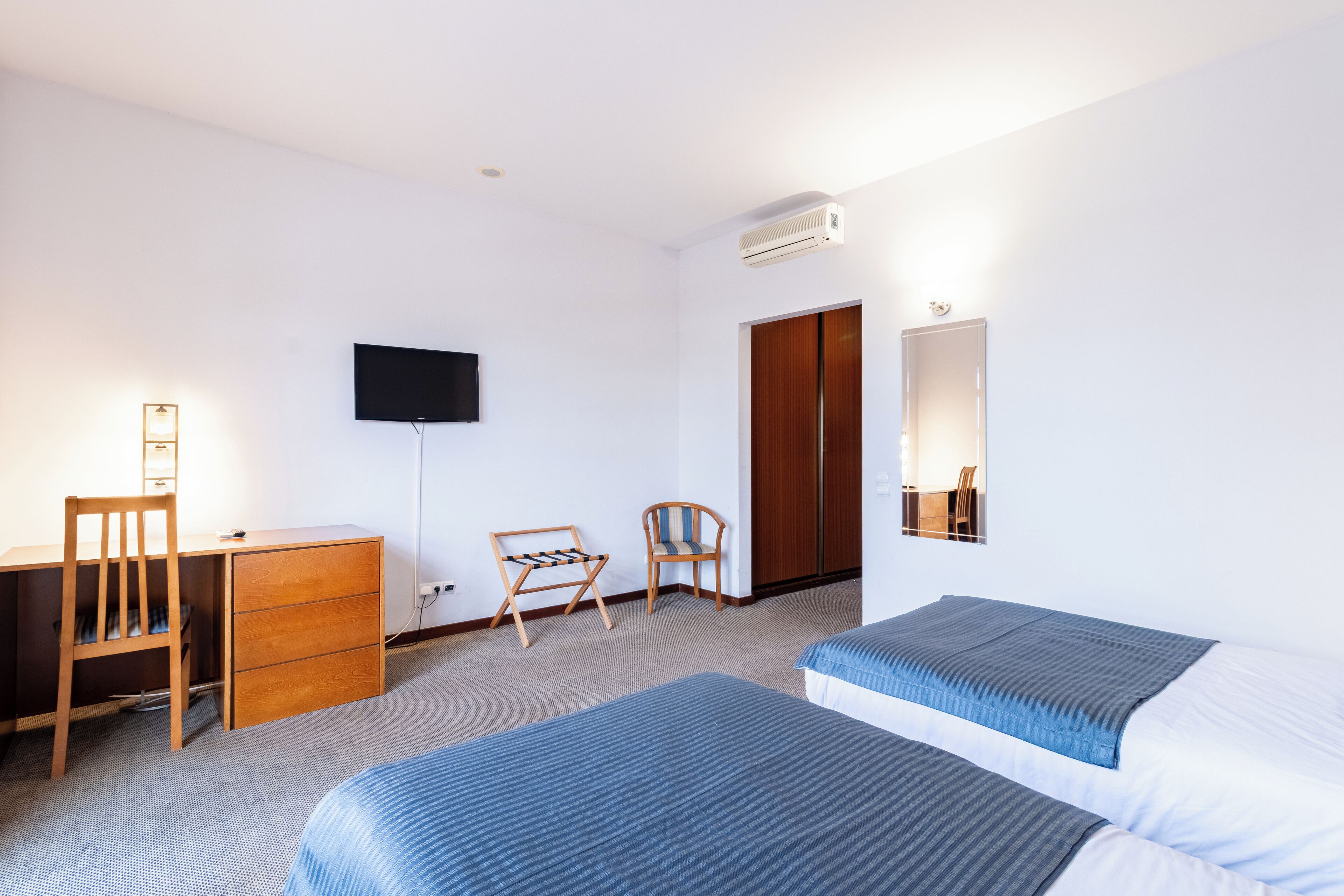 A hotel room with a bed, a desk with a chair, a TV, and a wardrobe.