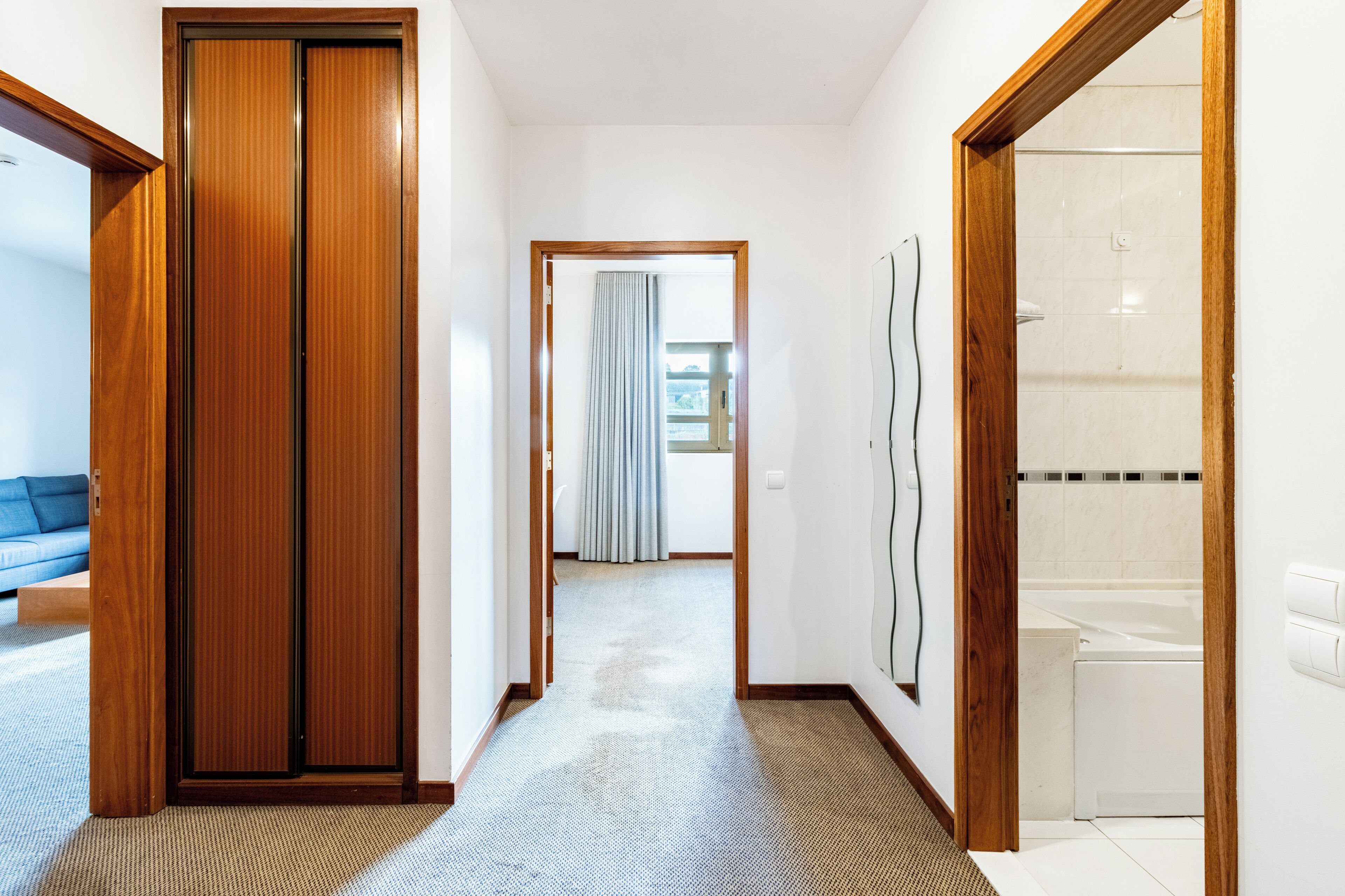 Een hal met een houten deur, een douchegedeelte en uitzicht op een kamer met een bed en een raam.