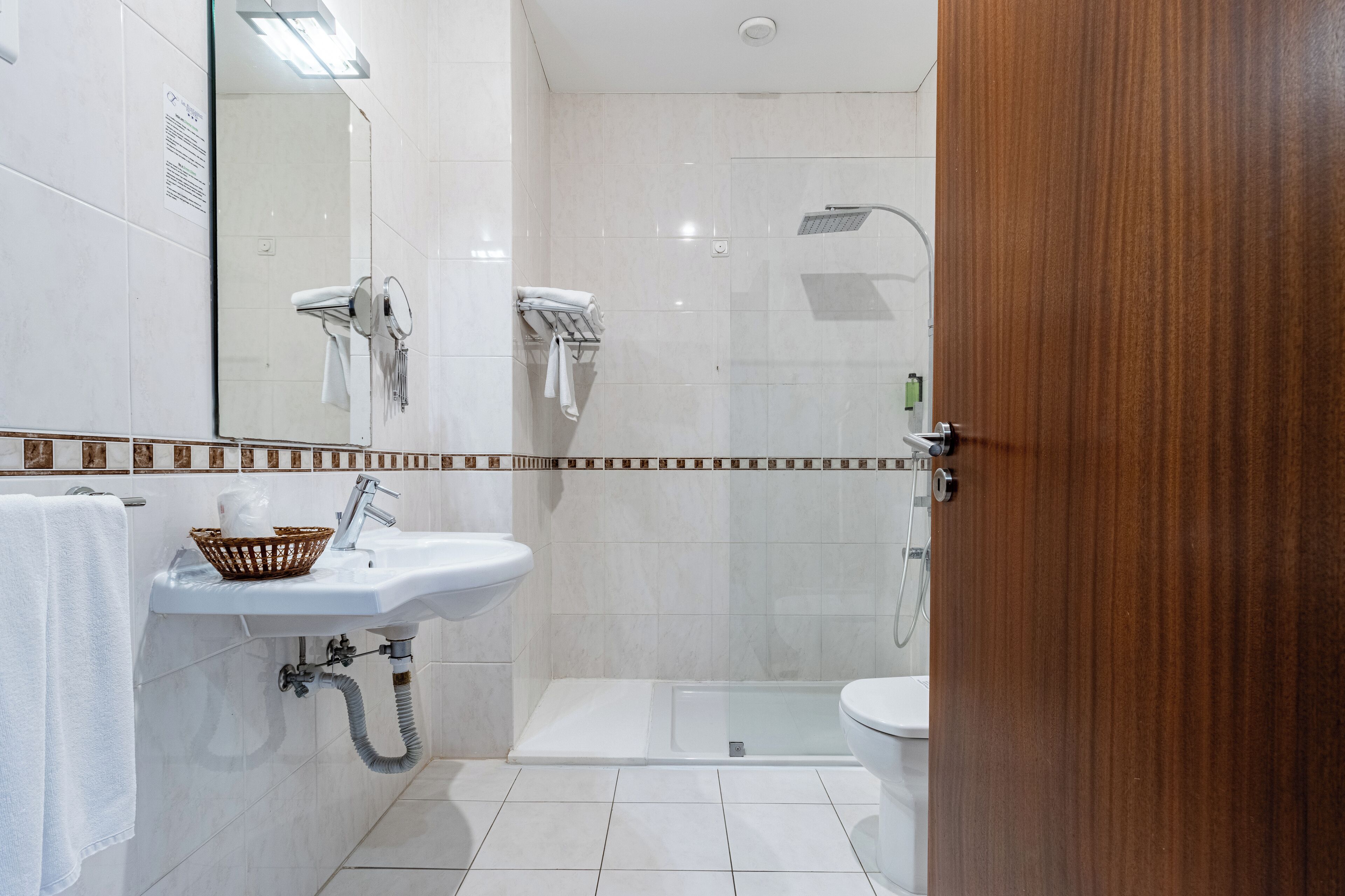 Un baño moderno con cabina de ducha de vidrio, un lavamanos blanco con una cesta y un inodoro.