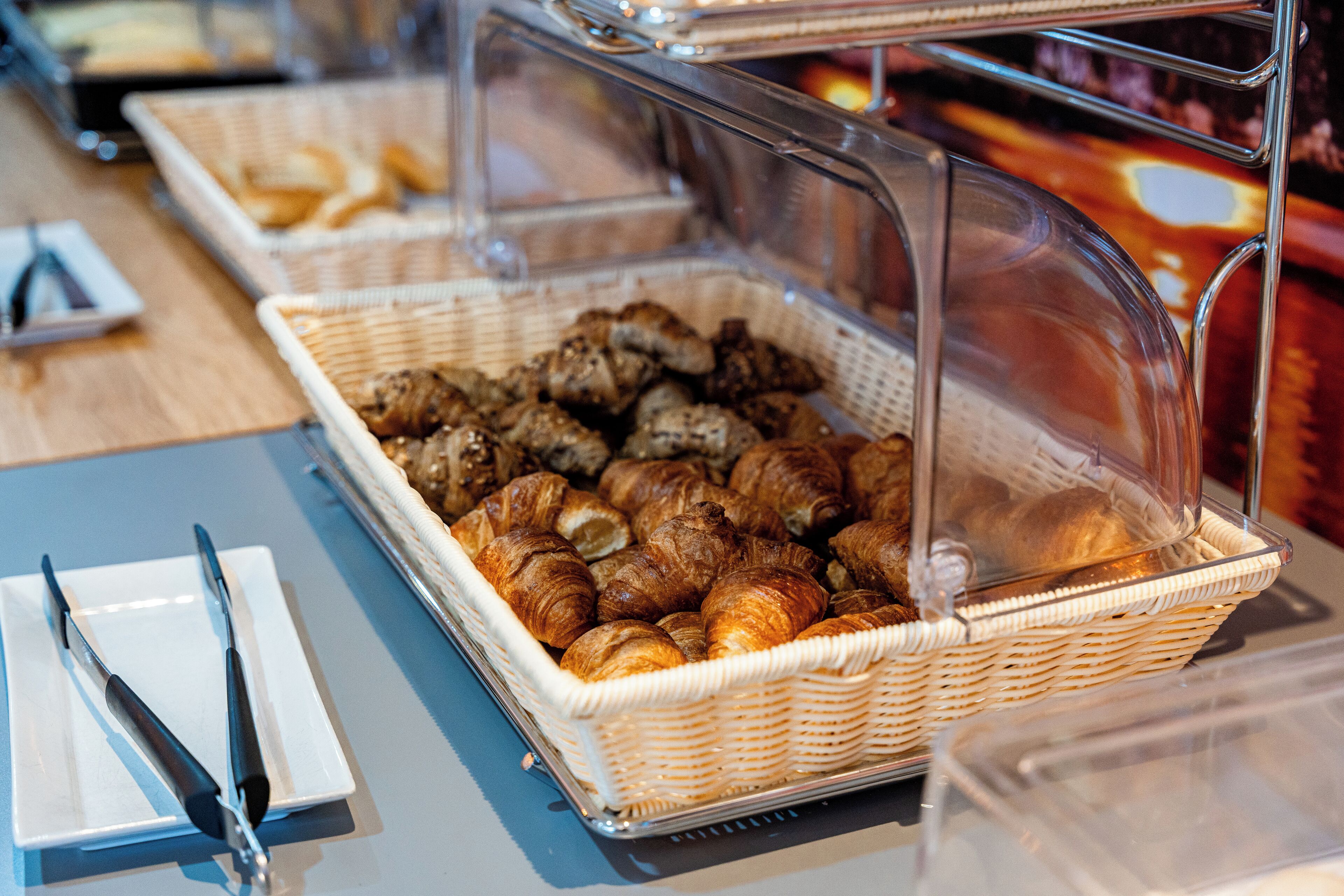 Ein Buffet mit Korbgebäck und einer transparenten Abdeckung.