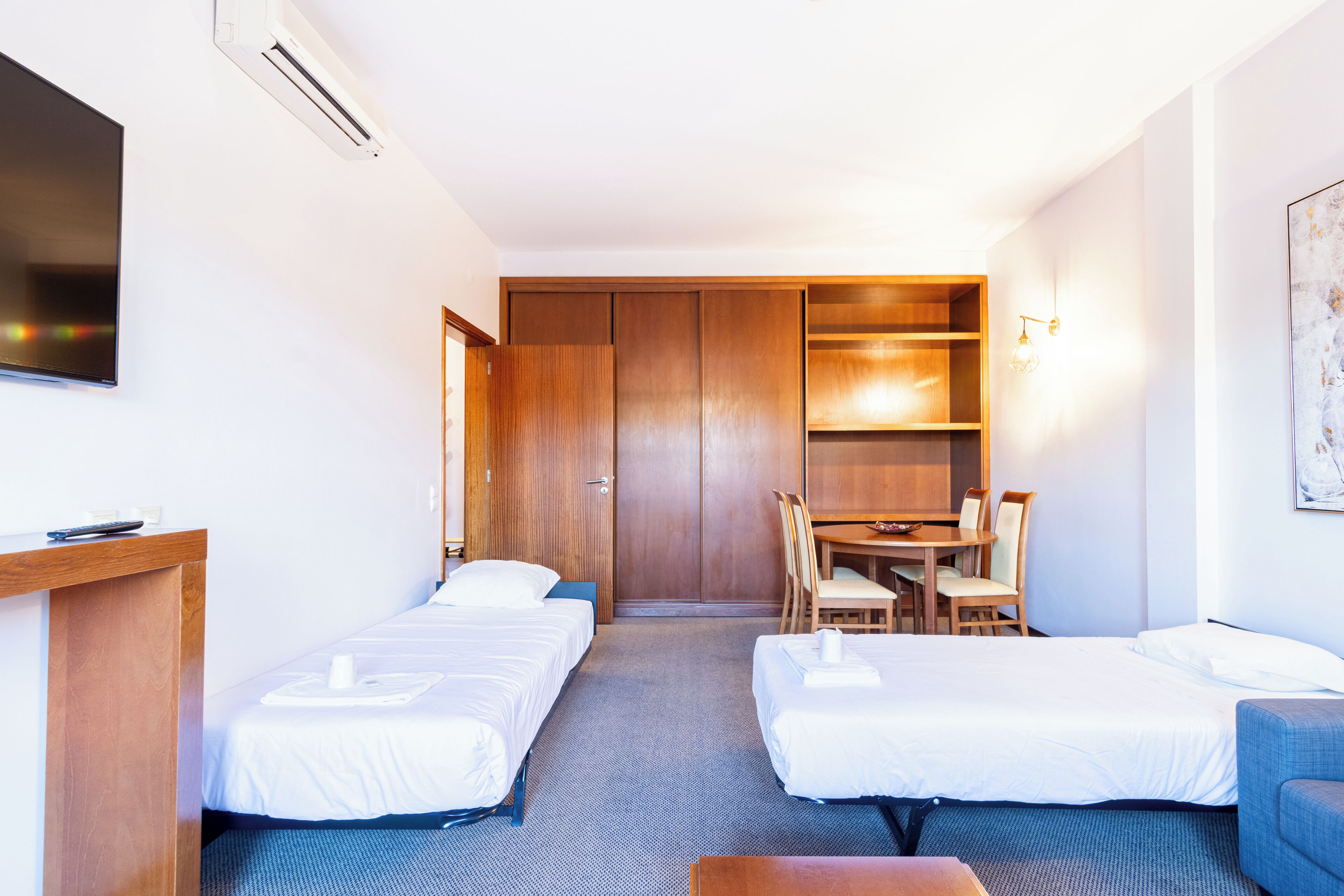 A hotel room with two single beds, a desk with a chair, a TV, and a wooden wardrobe.