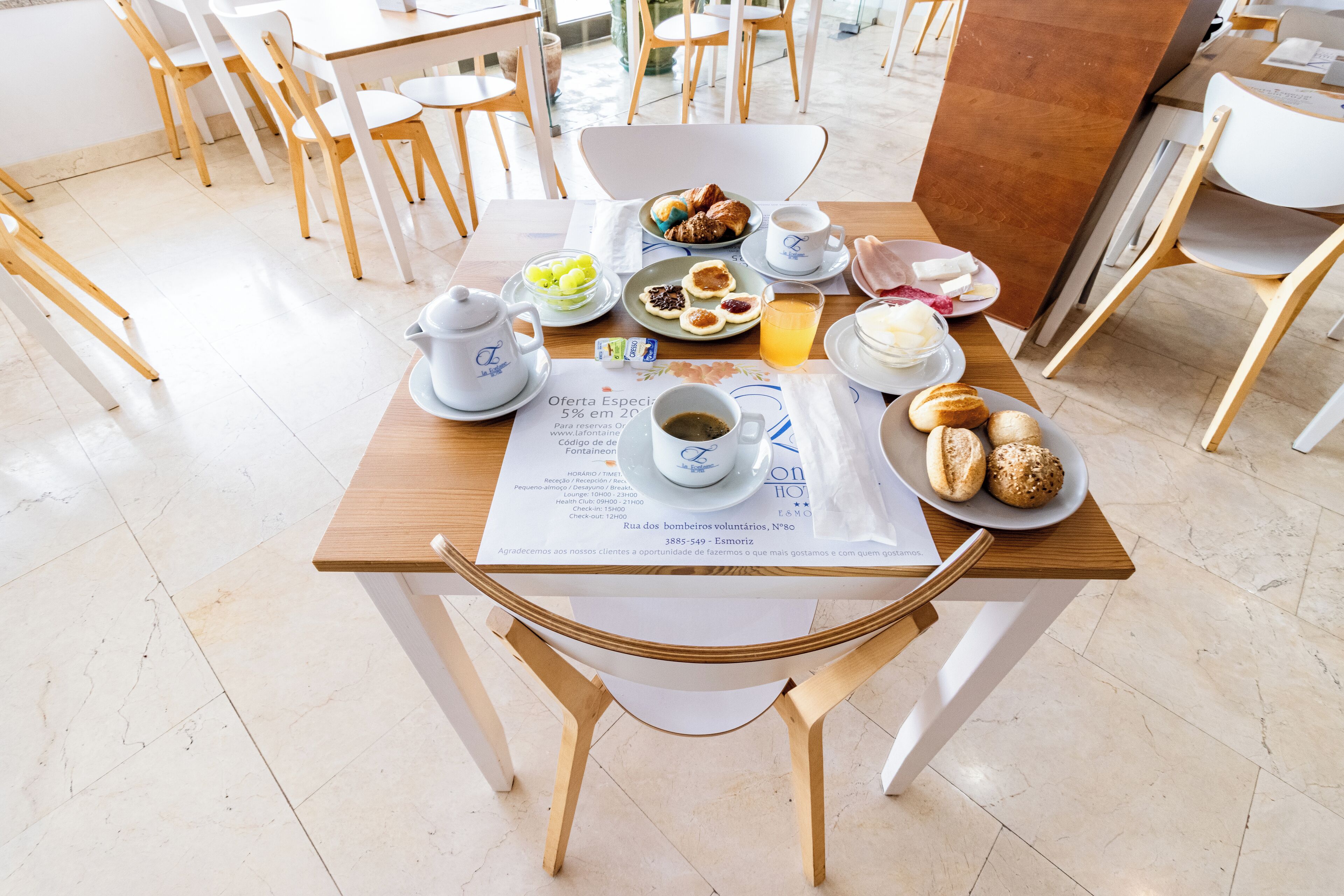 Uma mesa de café da manhã com um cardápio, uma xícara de café, doces e um copo de suco de laranja.