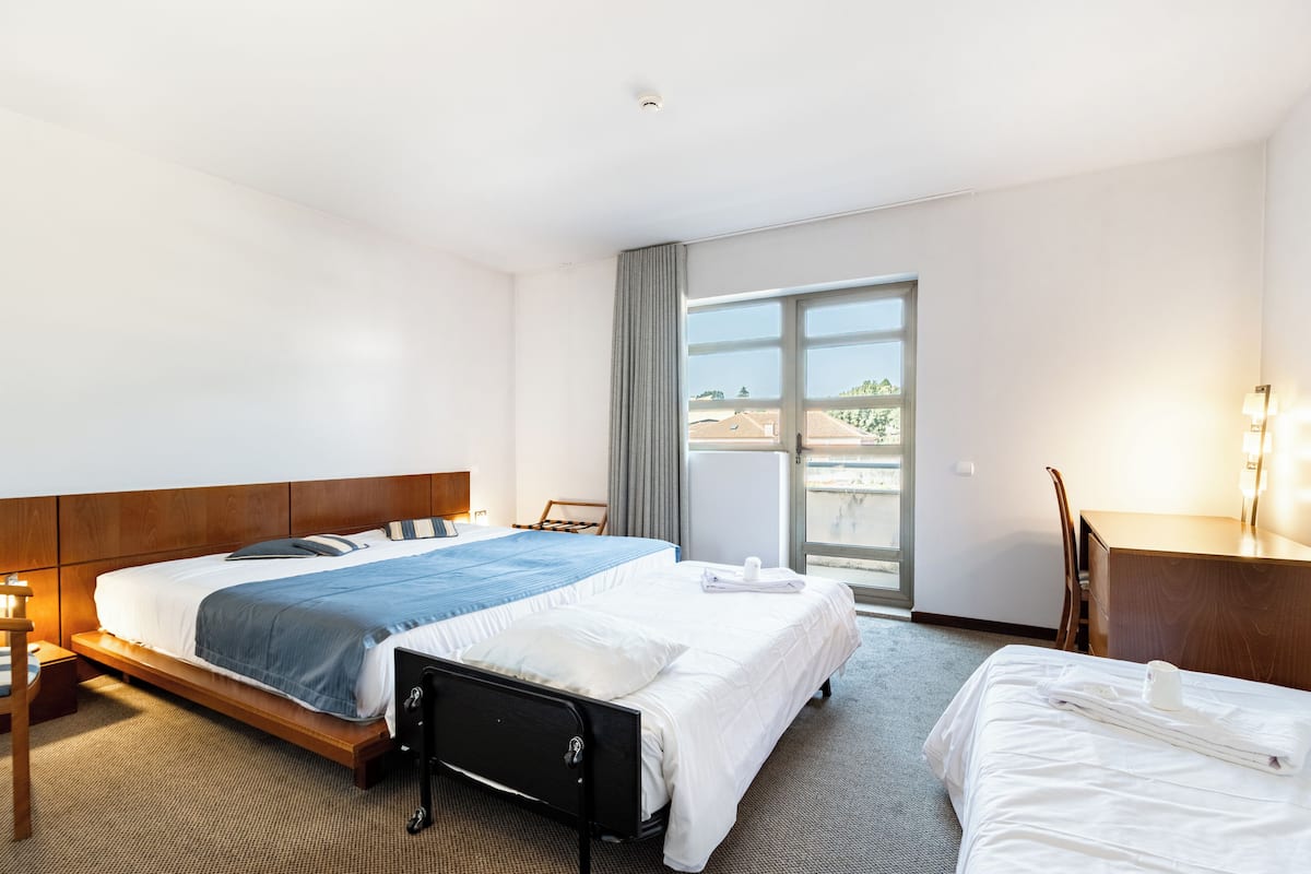 A hotel room with a large bed, a desk, a chair, and a view of the outside.