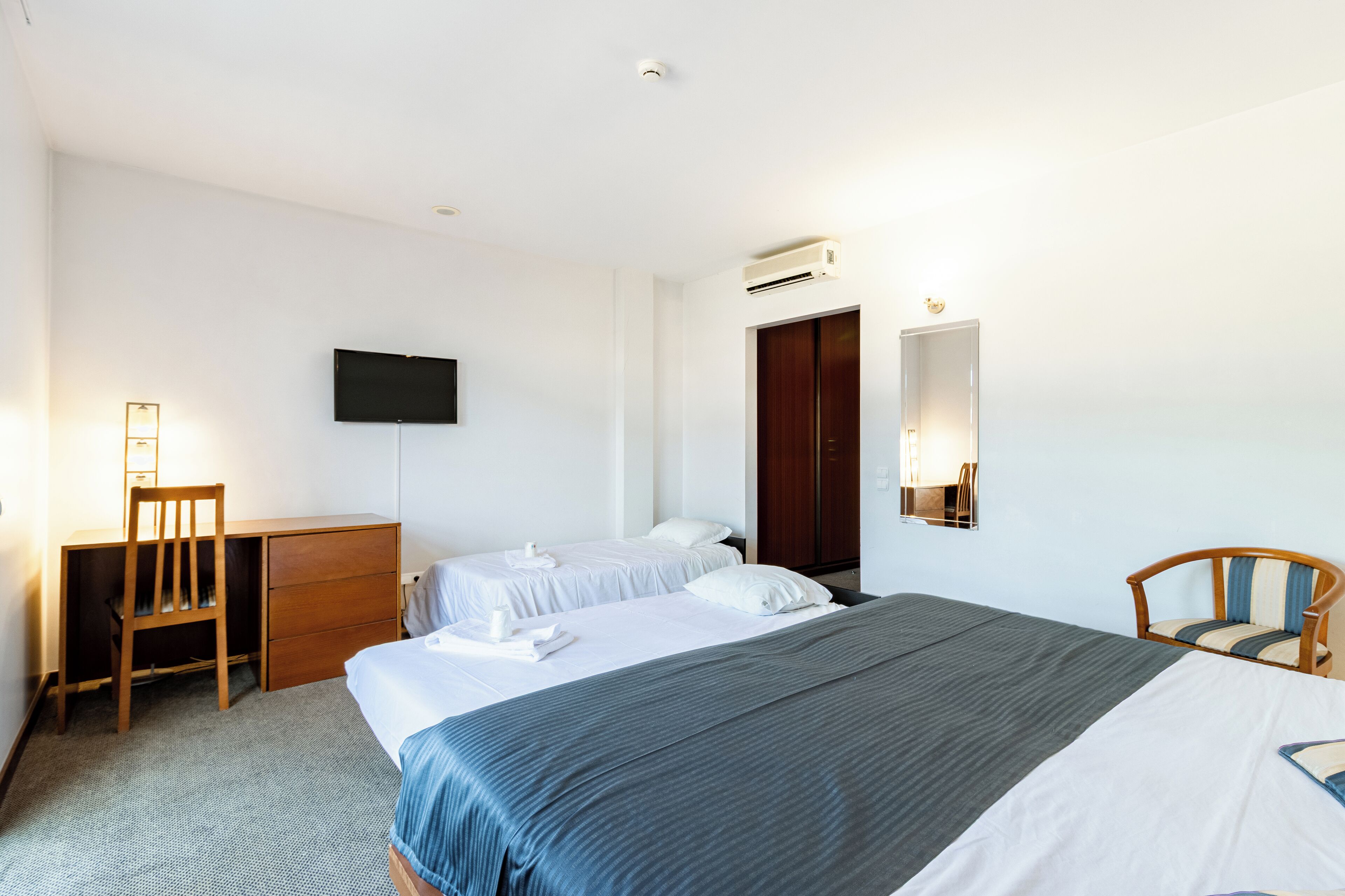 Una habitación de hotel con una cama grande, un escritorio, una silla, un televisor y un equipo de aire acondicionado.