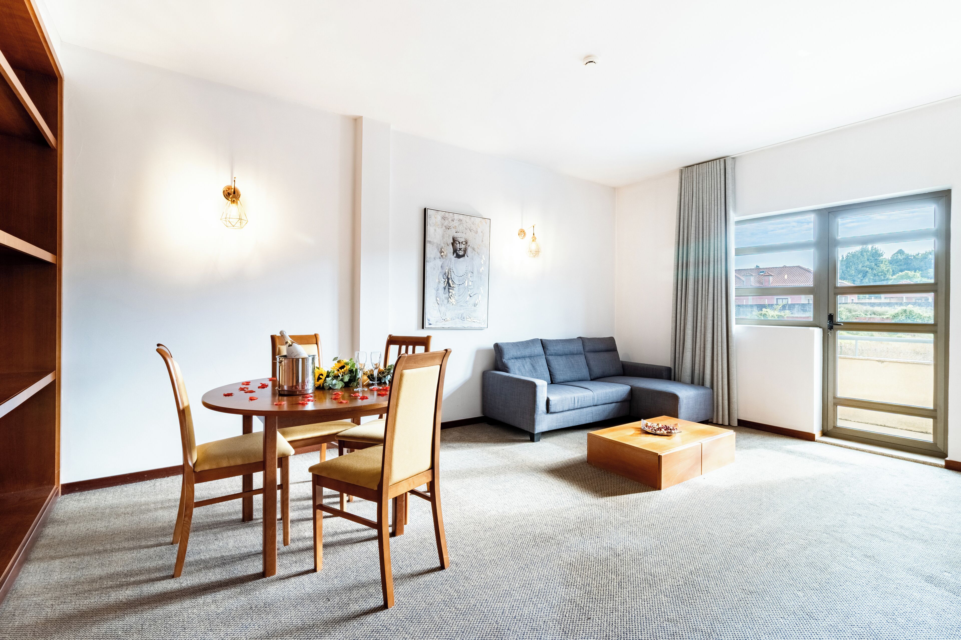 A modern hotel room with a dining area, a sofa, and a large window offering a view.