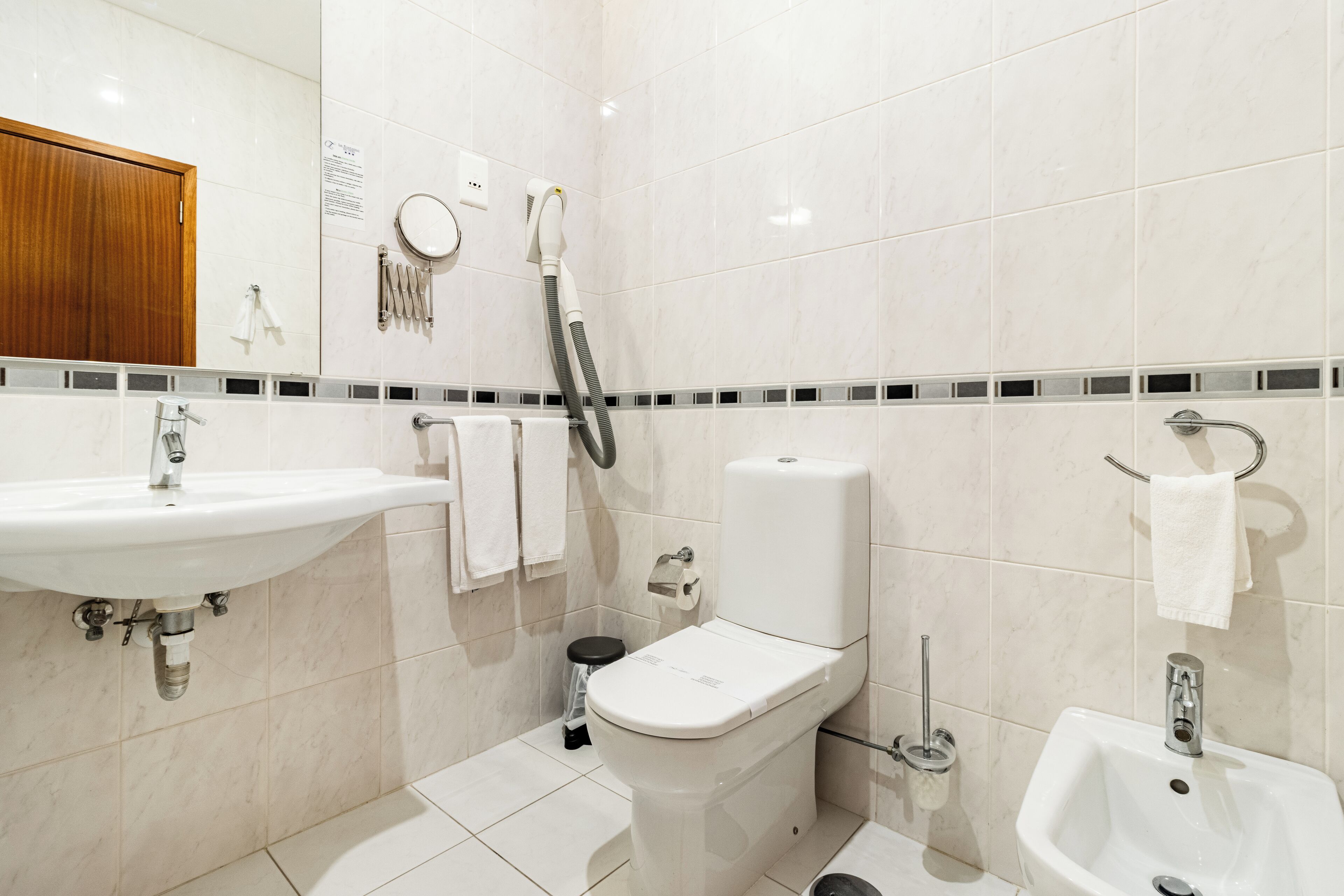 Ein modernes Badezimmer mit Toilette, Bidet, Waschbecken und einer Dusche mit Duschschlauch.
