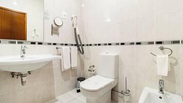 Ein modernes Badezimmer mit Toilette, Bidet, Waschbecken und einer Dusche mit Duschschlauch.