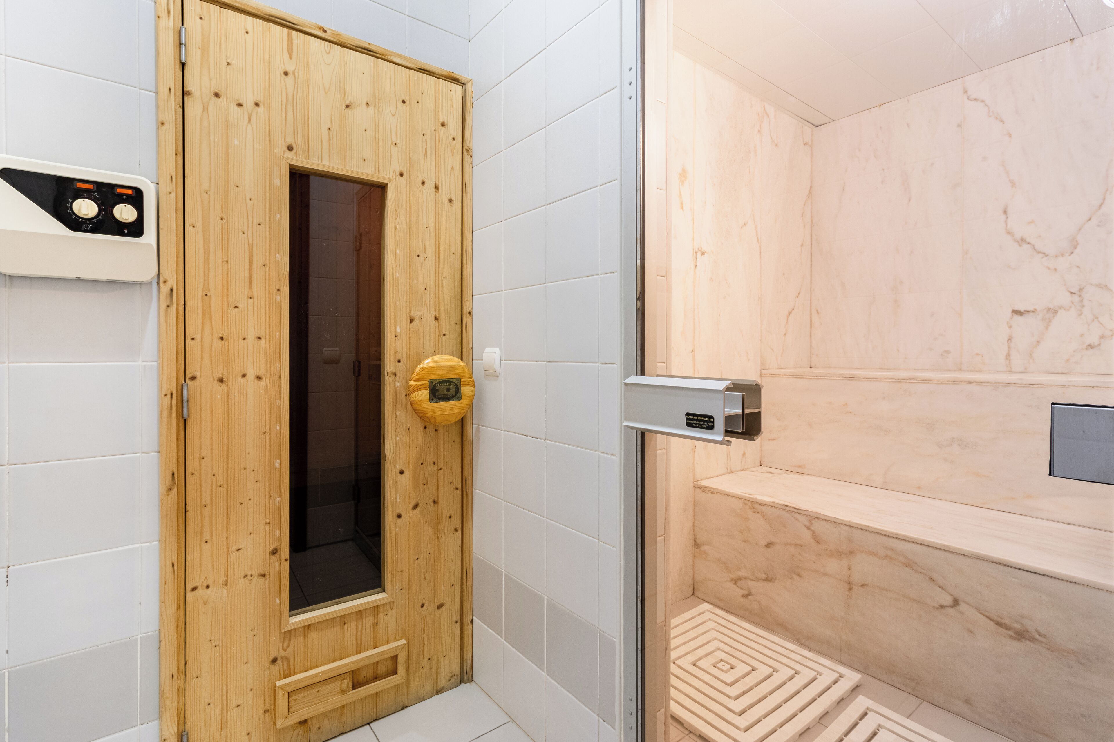 Un cuarto de sauna con puerta de madera, panel de control y pared de mármol.