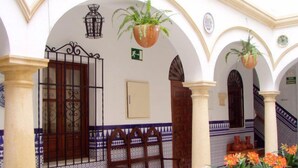 A courtyard with tiled walls, a wooden bench, hanging planters, and a staircase. - Maestre (Córdoba)