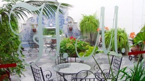 An outdoor patio area with round tables and chairs, surrounded by potted plants and a decorative metal structure. - Maestre (Córdoba)