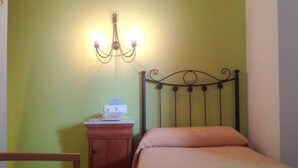 A bedroom with a bed, a wooden chair, a nightstand, and a wall-mounted lamp. - Maestre (Córdoba)