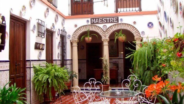 A courtyard with a sign reading "MAESTRE," surrounded by potted plants and a glass table. - Maestre (Córdoba)
