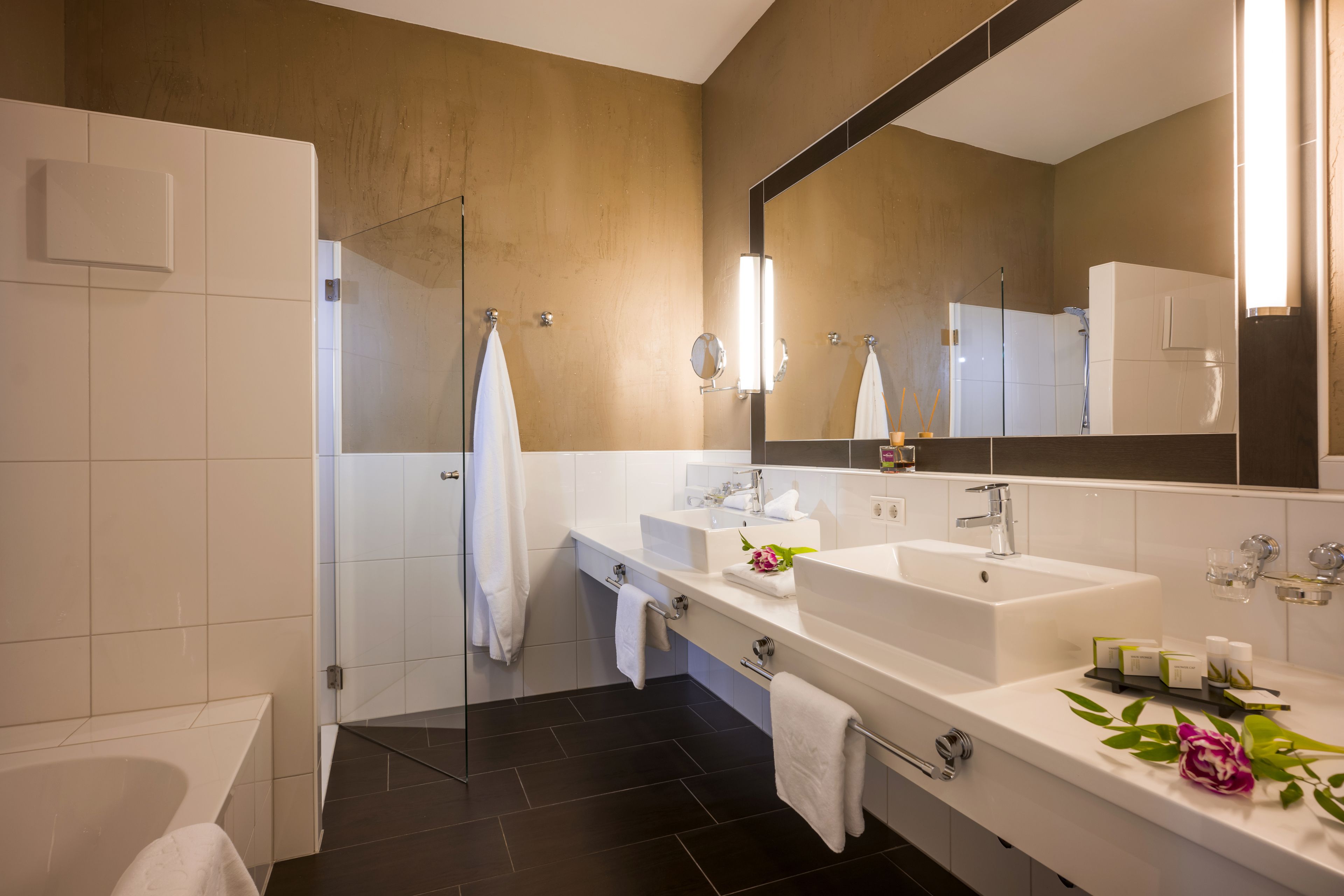 Une salle de bain moderne avec une douche à l’italienne en verre, deux vasques, un grand miroir et une baignoire.