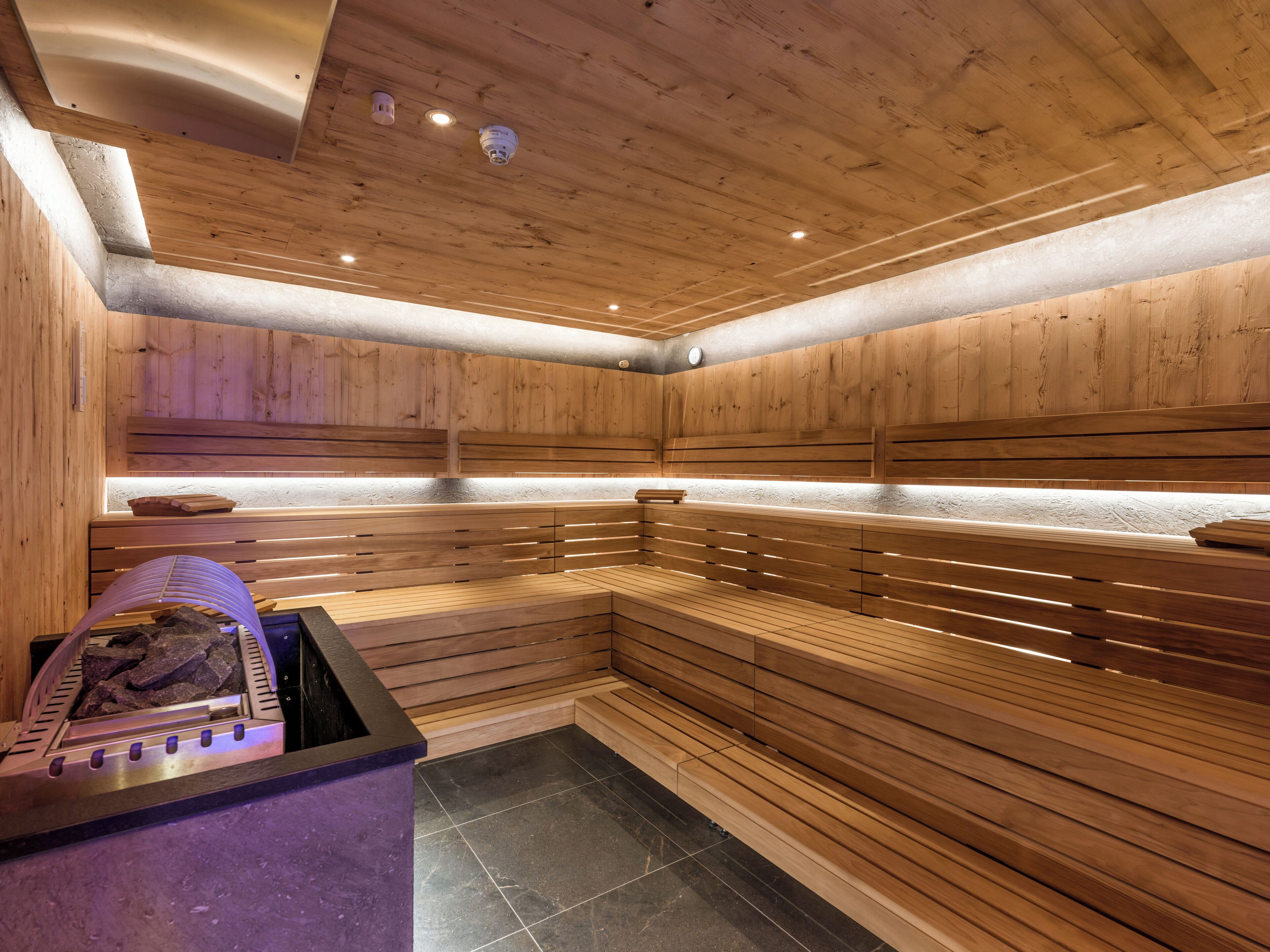 Eine Sauna mit Holzbänken, einem Steinfußboden und einer Steinsitzbank mit Handtuch.