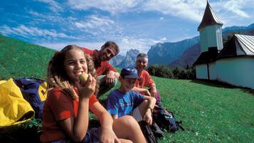 A group of people sitting on grass with a church and mountains in the background.