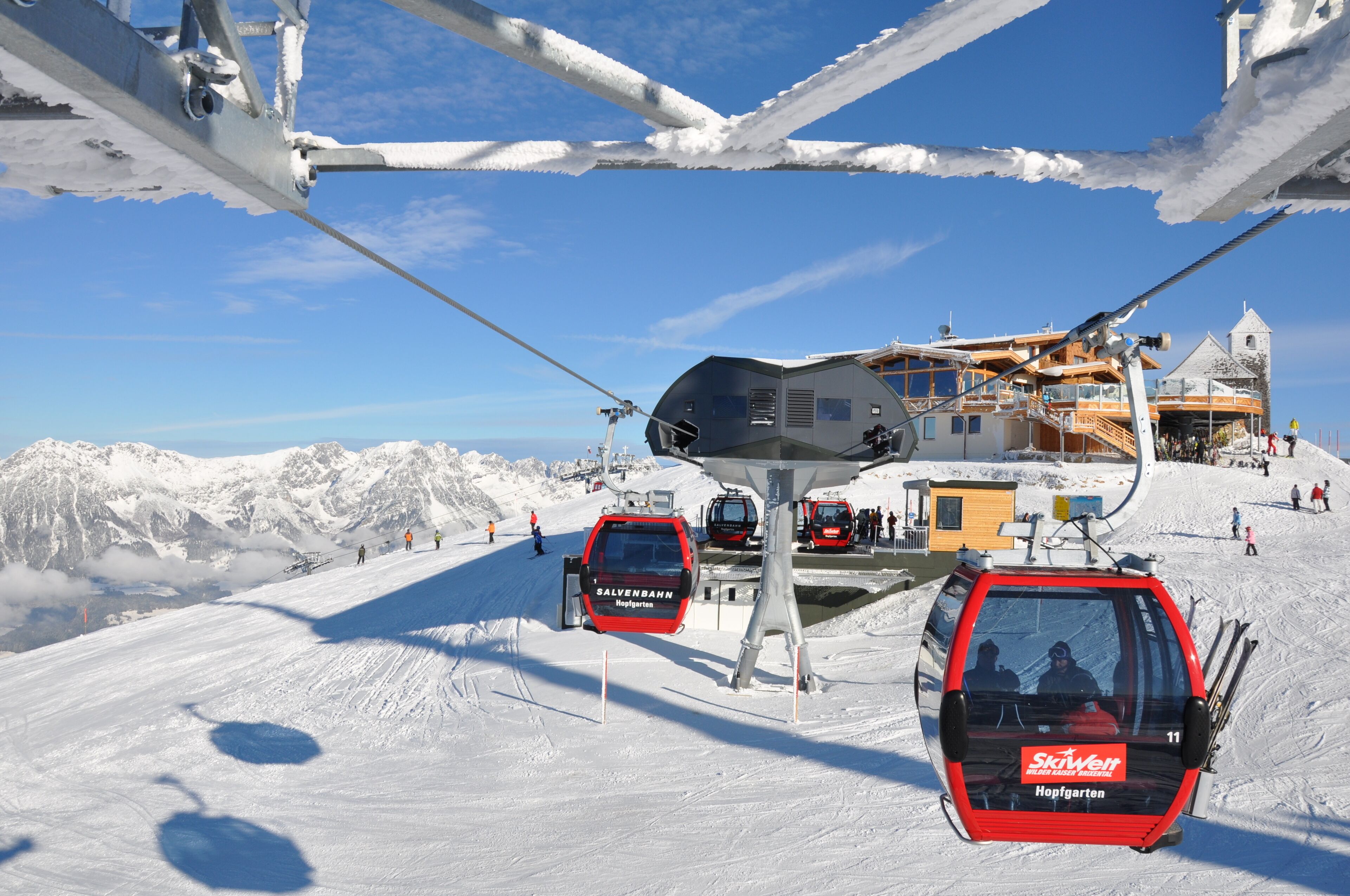 A ski lift with cabins and a cable system against a snowy mountain backdrop.