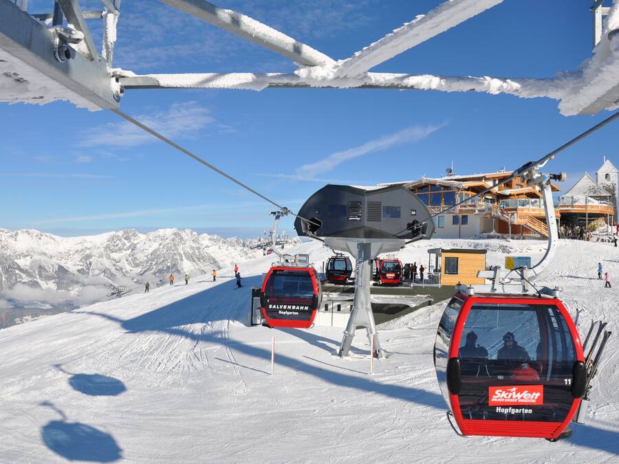 A ski lift with cabins and a cable system against a snowy mountain backdrop.