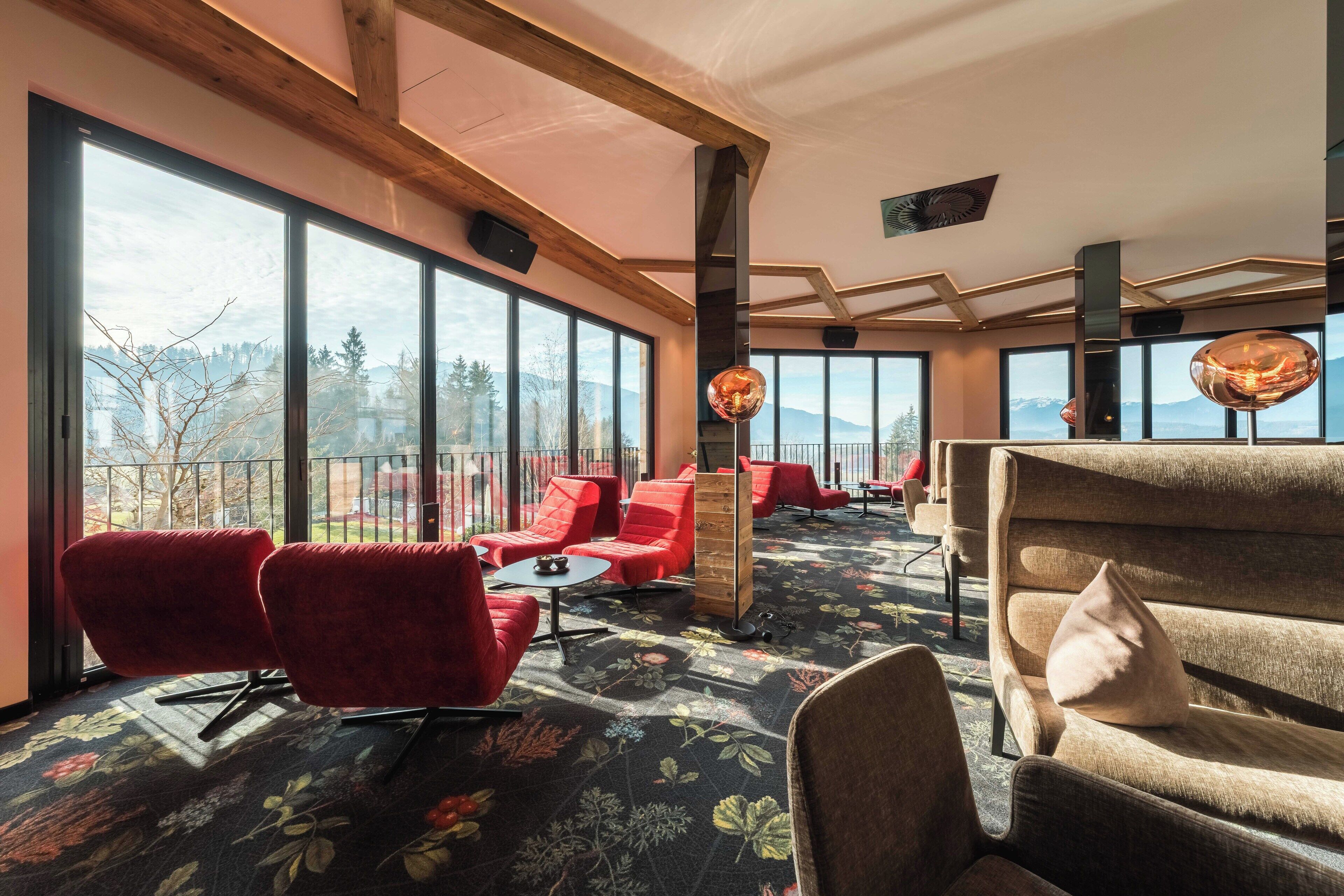 Una habitación amplia con ventanas grandes, asientos en rojo y beige, y una alfombra estampada con flores.