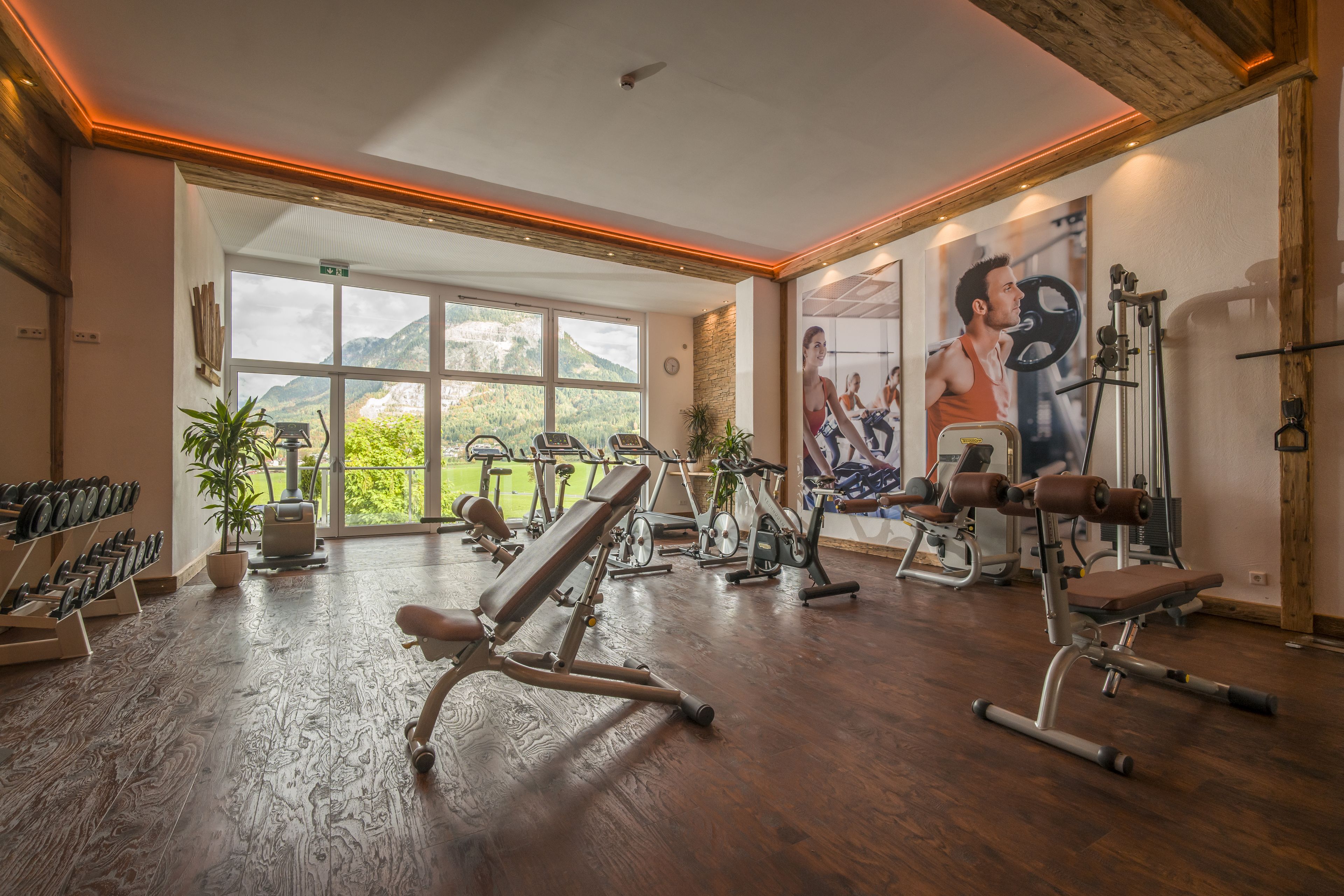 A gym with various exercise equipment, large windows, and a view of mountains.