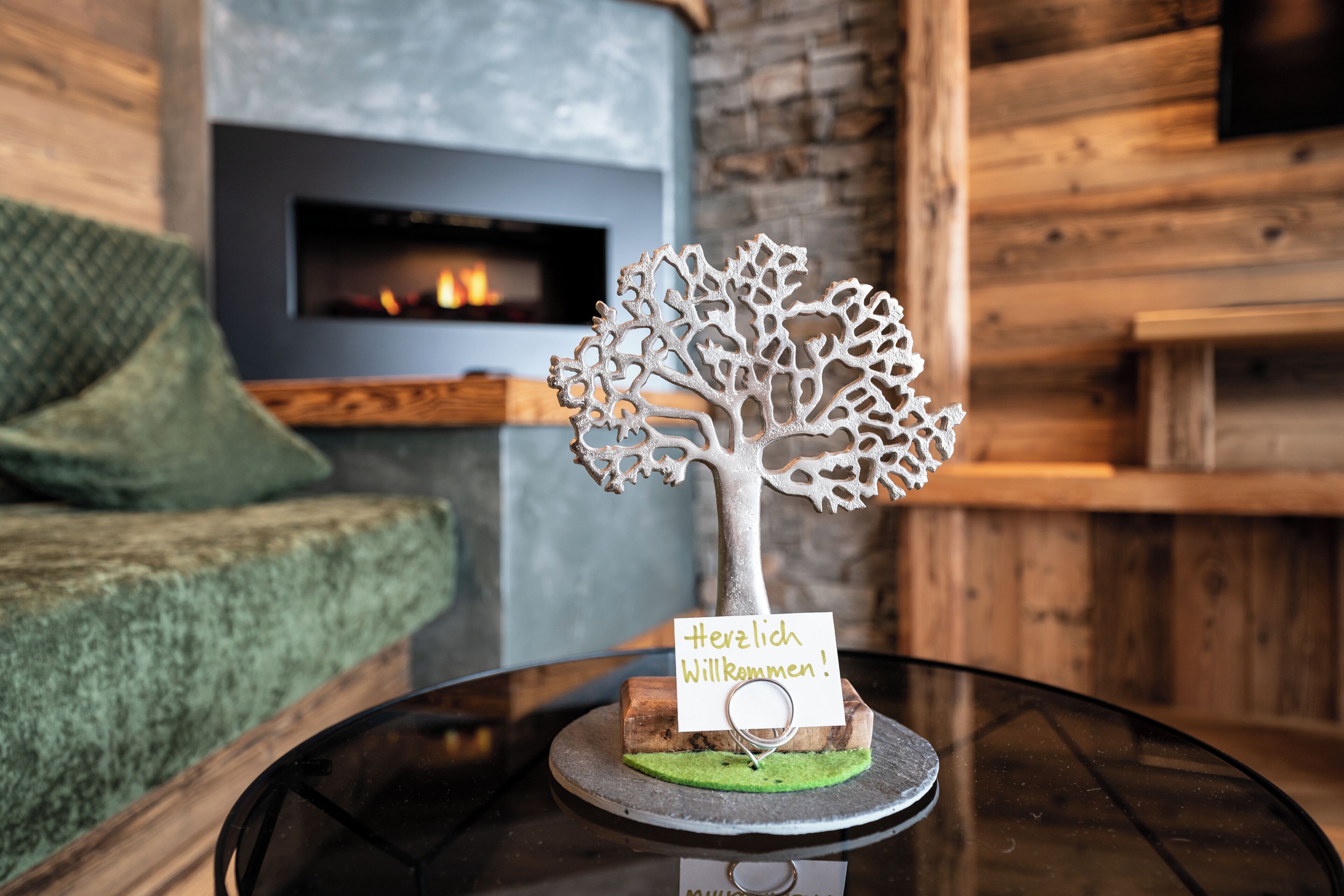 A decorative tree with a sign on a table in a room with a fireplace and wooden walls.