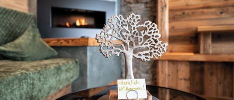 A decorative tree with a sign on a table in a room with a fireplace and wooden walls.