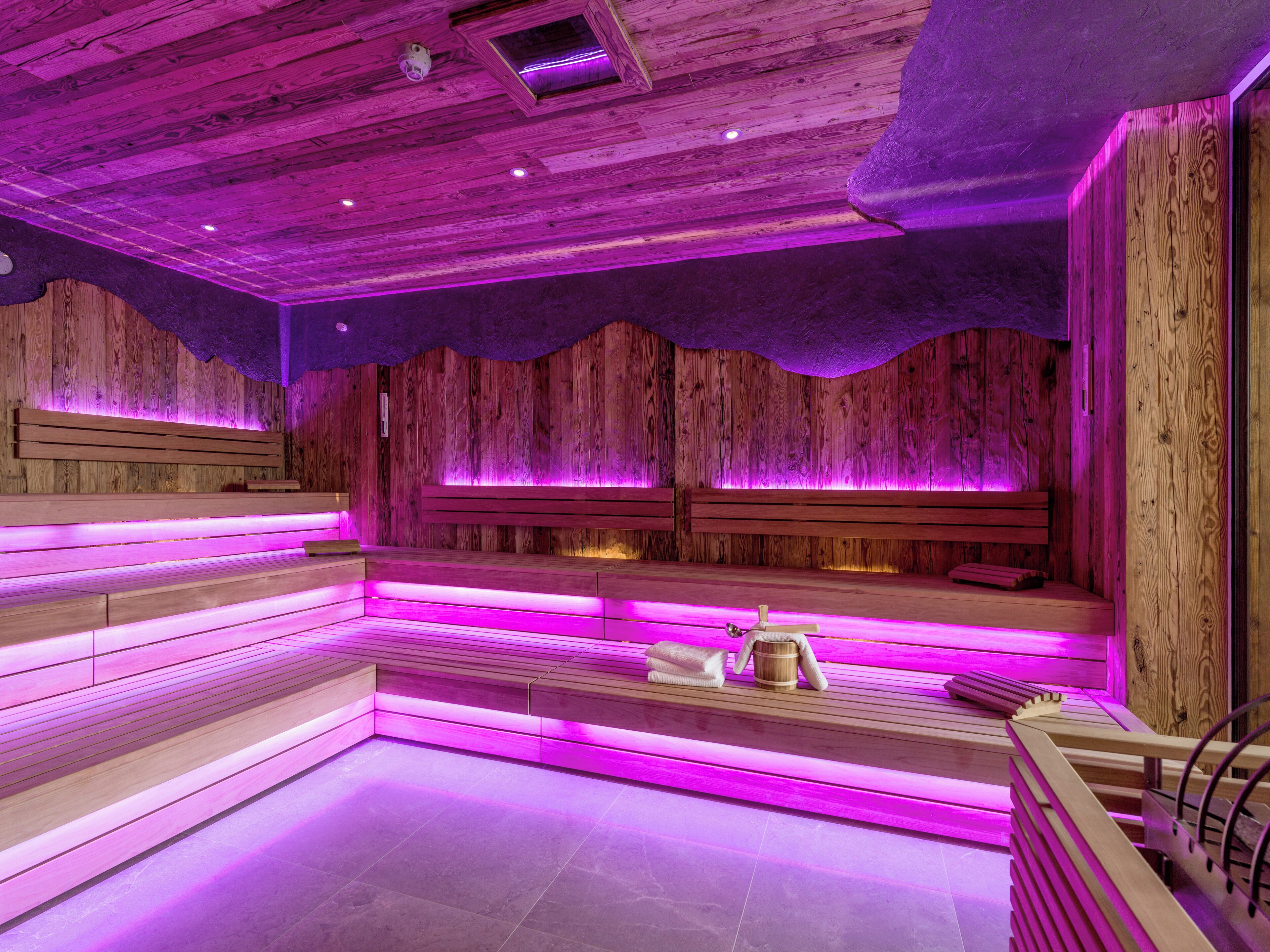 Un sauna en bois, doté de bancs et d’une banquette, éclairé par un éclairage violet.