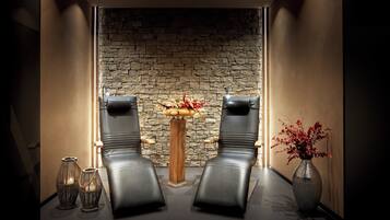 Un espace spa comprenant deux fauteuils en cuir noir, un mur en pierre, une table en bois ornée d’un vase de fleurs et deux vases décoratifs.