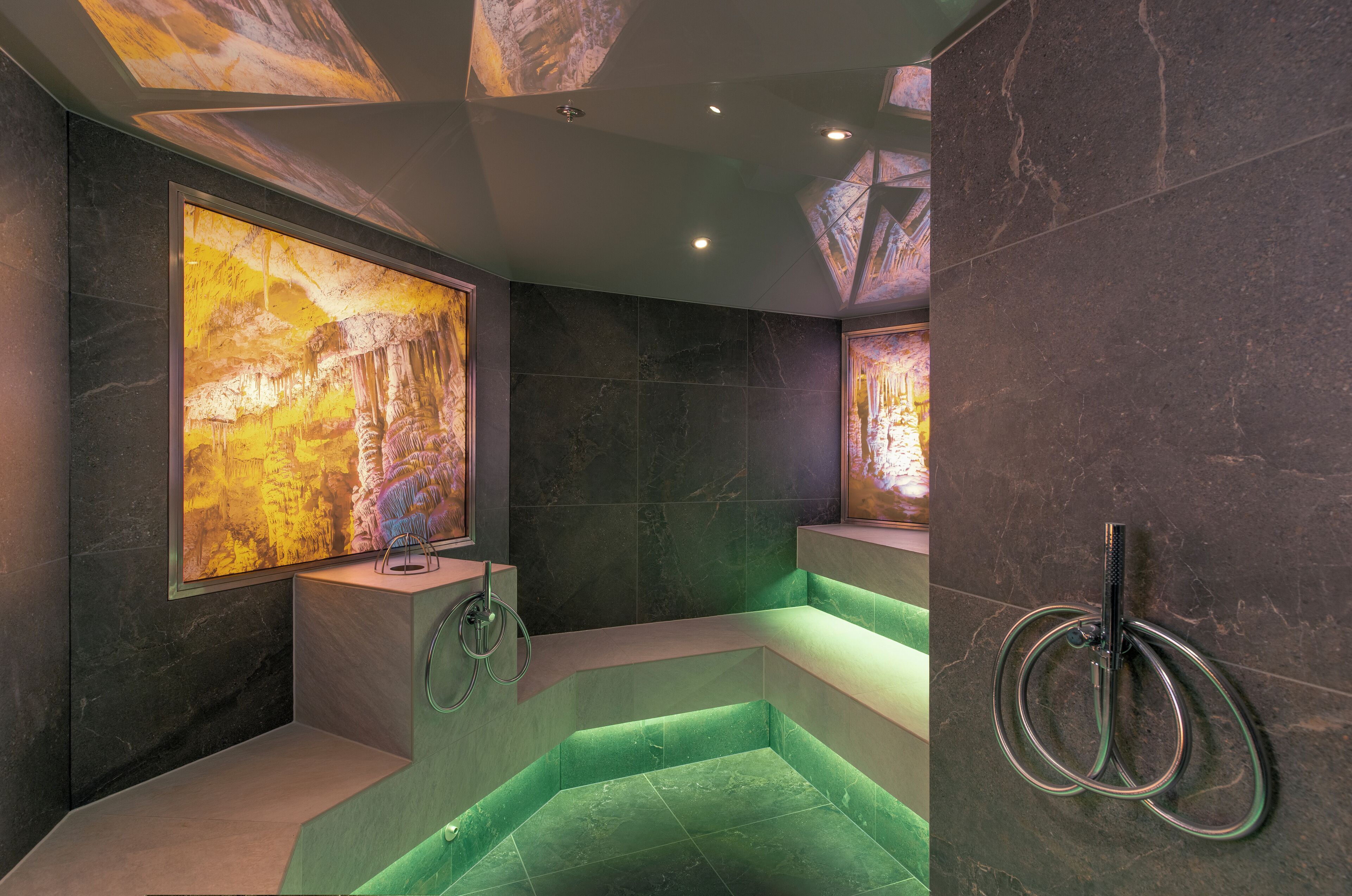 A modern bathroom with a green heated floor, marble walls, and a large framed picture of a cave.