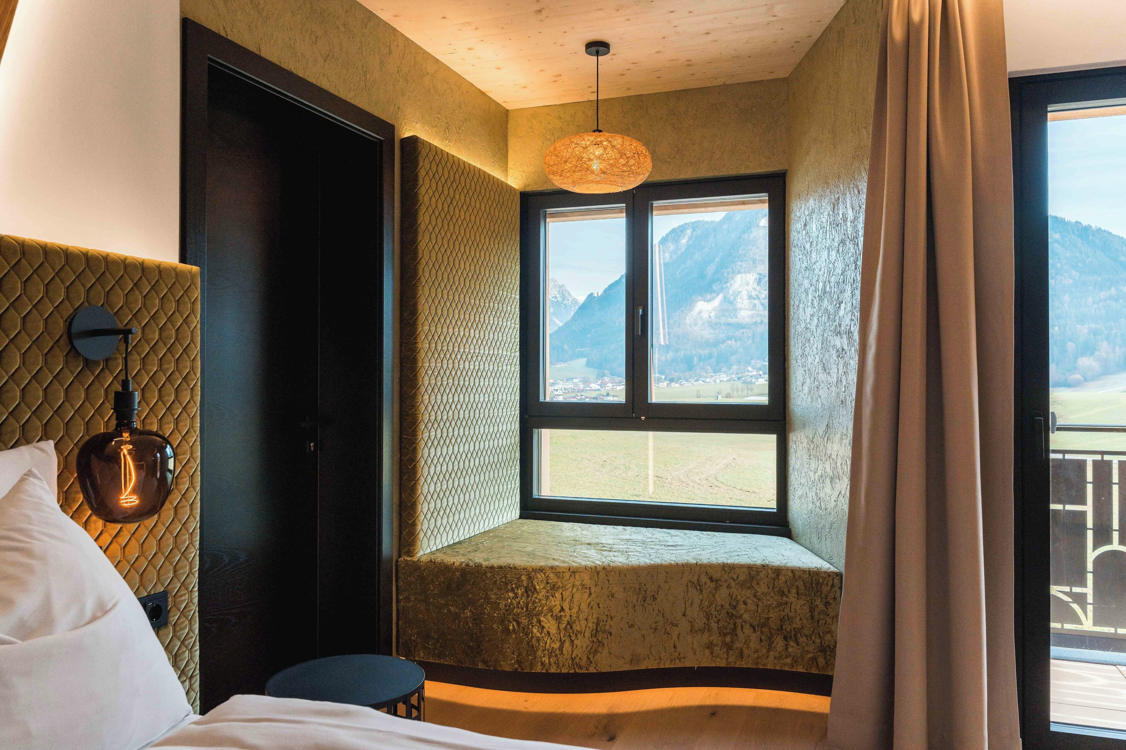 A room with a bed, a window with a mountain view, a textured wall, and a hanging light fixture.
