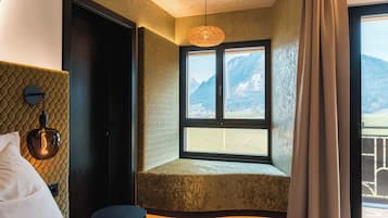 A room with a bed, a window with a mountain view, a textured wall, and a hanging light fixture.