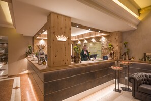 Un área de recepción con un mostrador de madera, un espacio de espera con un sofá y un fondo de pared de piedra.