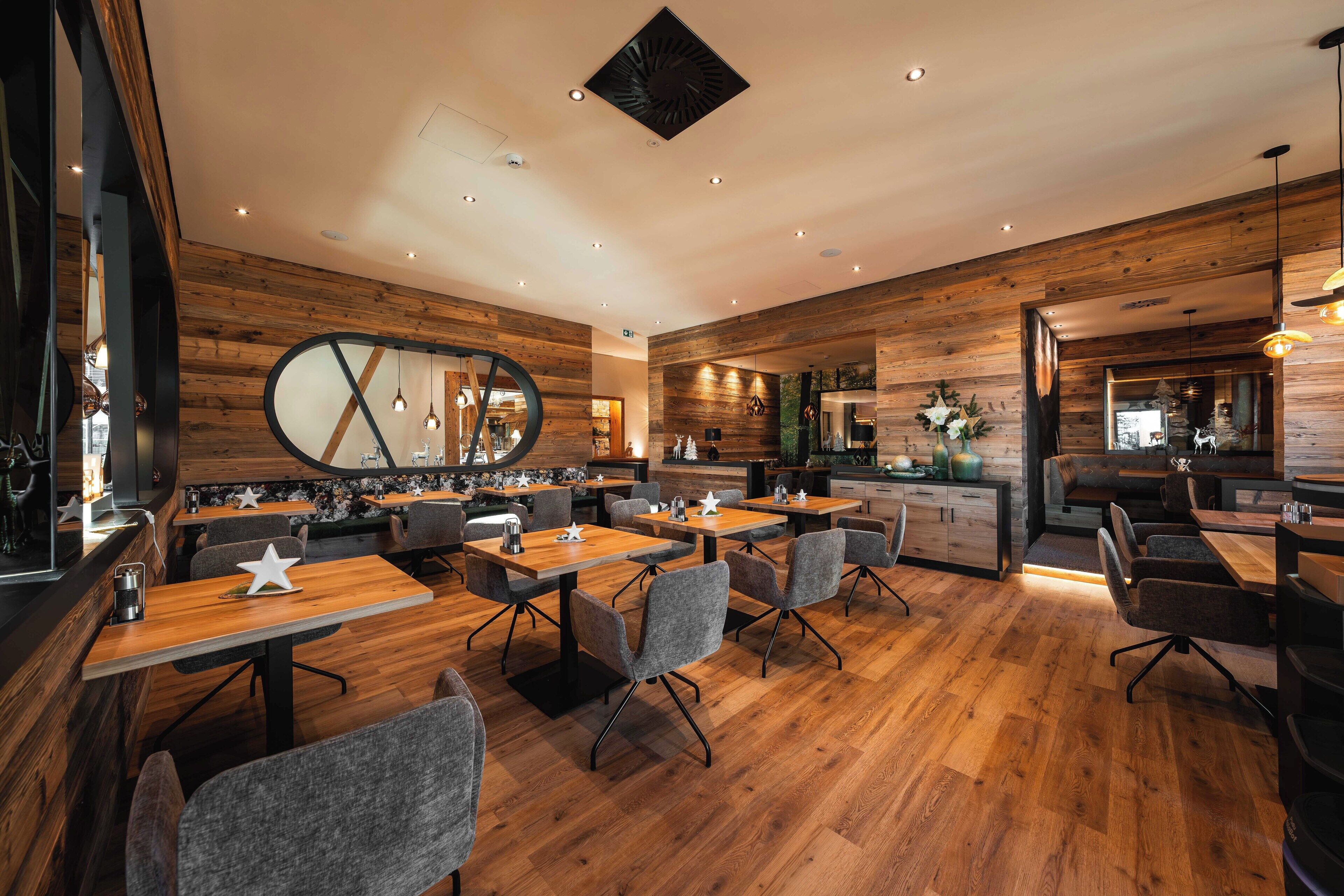 A modern restaurant with wooden walls and a central bar area. Tables are arranged for dining, and there are chairs and a counter with a mirror.