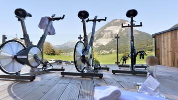 Three stationary bikes on an outdoor deck with a mountain view.