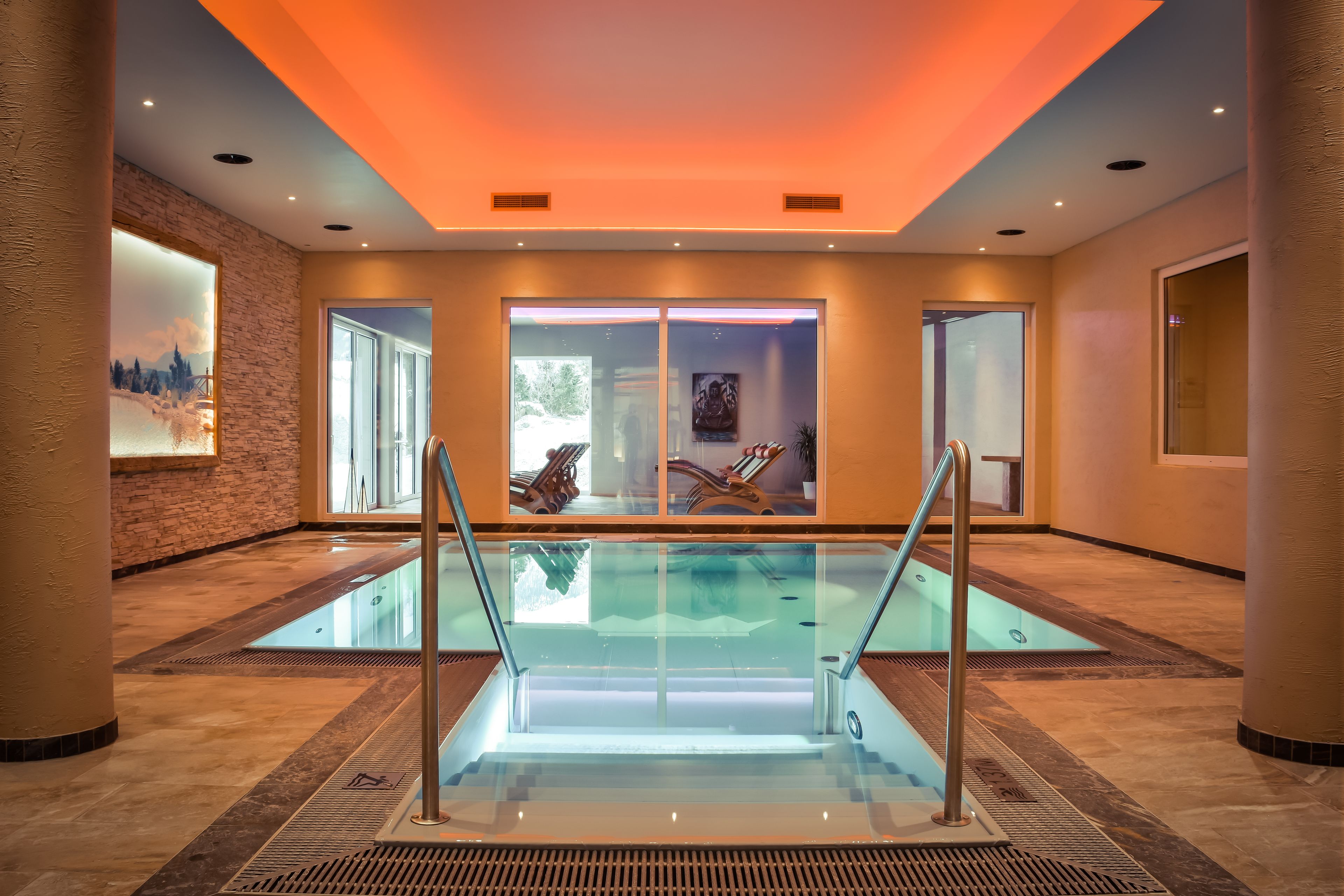 A modern indoor pool with glass railings, large windows, and a warm ceiling light.