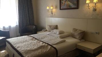 Habitación de hotel con una cama grande, dos mesitas de noche, una silla, un cuadro en la pared y una ventana con cortinas.