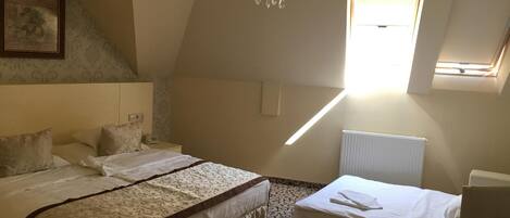 A bedroom with two beds, a chandelier, a window, and a radiator.