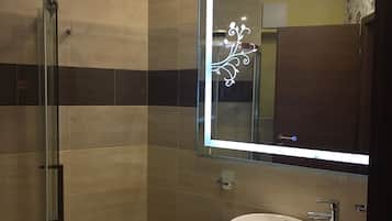 Une salle de bain moderne avec une douche à parois de verre, un lavabo blanc et un miroir agrémenté d’un éclairage décoratif.