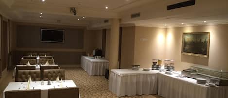 A banquet hall with multiple tables, a buffet area, and a painting on the wall.
