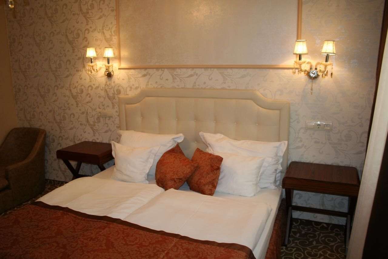 A neatly made bed with white and brown bedding, two bedside tables, and wall-mounted lamps.