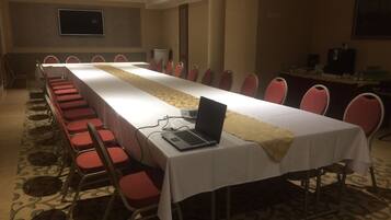 A conference room with a long table, red chairs, a laptop, and a projector.