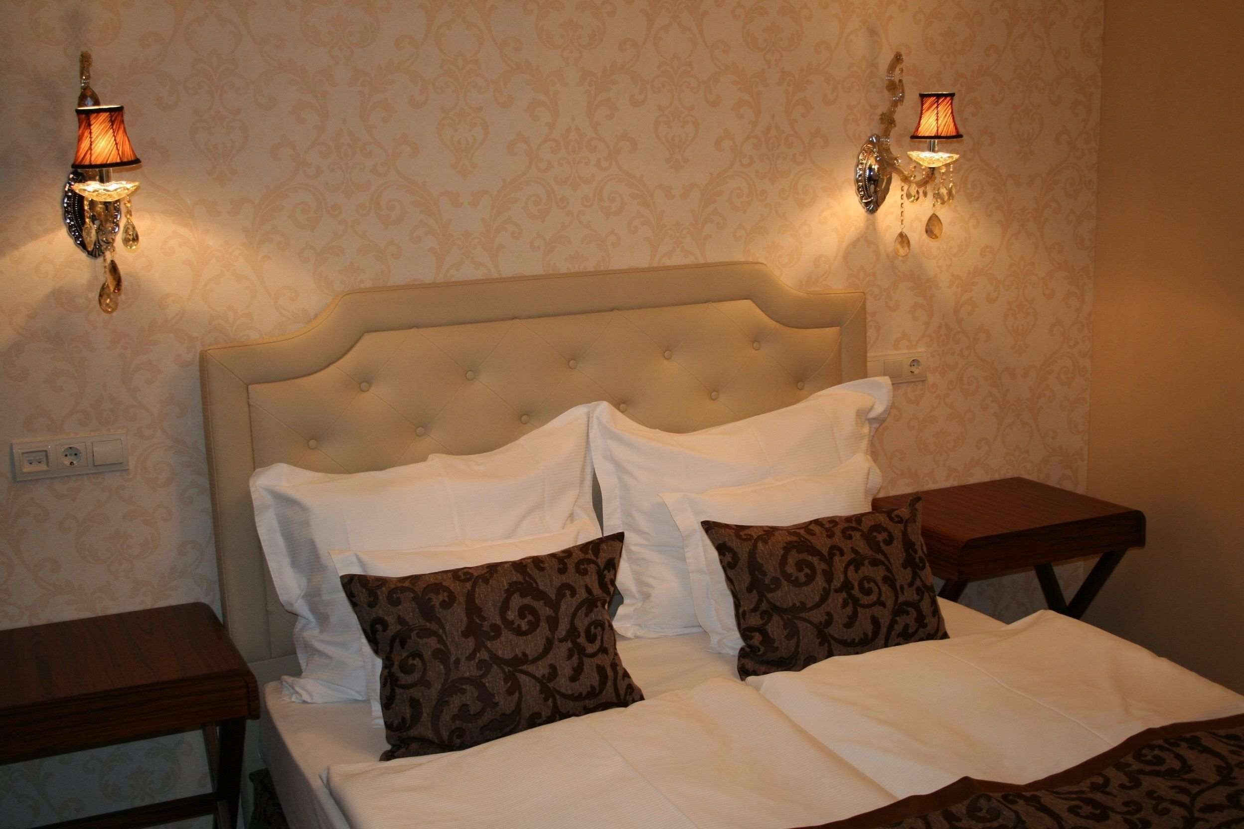 Una cama bien hecha con cabecera capitonada, dos mesitas de noche y lámparas de pared.
