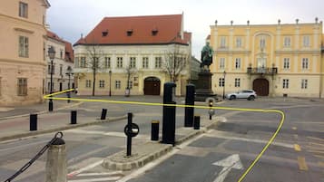 A street intersection with a statue, bollards, and buildings with classical architecture.